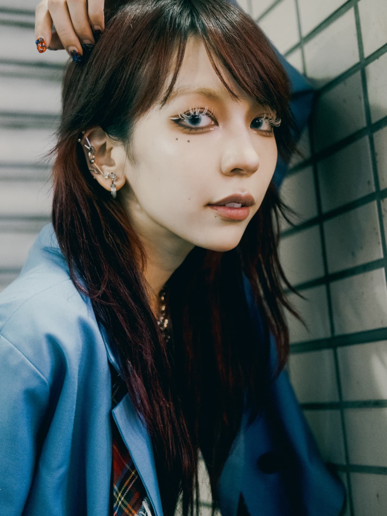水色のジャケットを着てタイル壁の前で振り返る女性のポートレート
